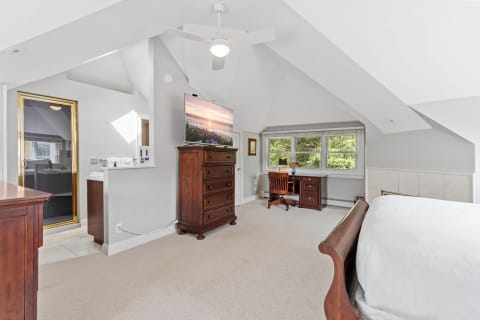 Spacious bedroom suite with vaulted ceiling, wooden furnishings, television, workspace, and natural light.