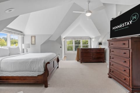A spacious bedroom featuring vaulted ceilings, a king-sized bed, and a dresser with a TV.