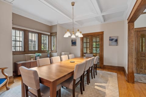 A spacious dining room with a long wooden table, upholstered chairs, and natural light flowing in from large windows.