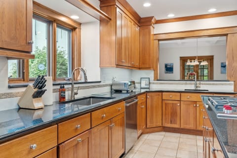 A kitchen with wooden cabinets and granite countertops, featuring modern appliances and a view of greenery outside.