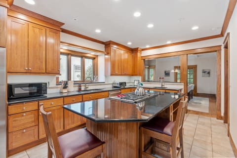 A modern gourmet kitchen featuring wooden cabinets, a black granite island, and dining area beyond.