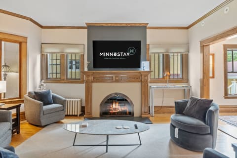 A bright and stylish living room with a fireplace, plush seating, and a wall-mounted TV.