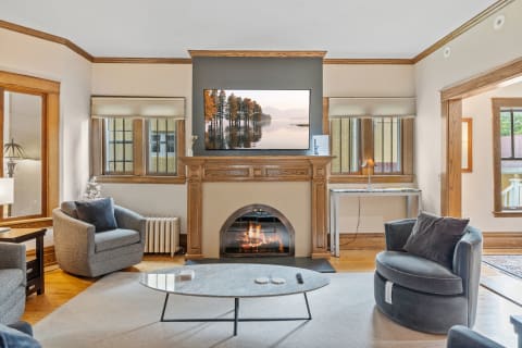 A modern living room with gray chairs, a marble coffee table, and a fireplace featuring a landscape image on the TV.