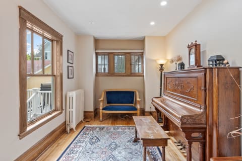 A living room featuring hardwood floors, an antique piano, a blue loveseat, and a decorative rug.