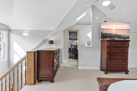 A spacious loft bedroom with vaulted ceilings, wooden dresser, and wall-mounted TV displaying a sunset.