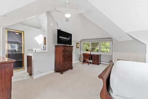 A spacious master suite featuring vaulted ceilings, a wooden dresser, and a workspace with natural lighting.