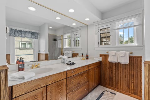 A spacious bathroom featuring a marble vanity, oak cabinetry, and a glass shower, illuminated by natural light.