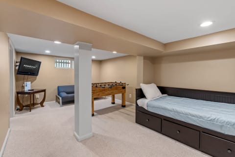 A well-decorated basement entertainment area with a bed, foosball table, and television.
