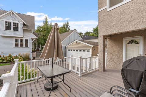 A wooden deck with a table and umbrella overlooks a neat neighborhood with houses and a garage.