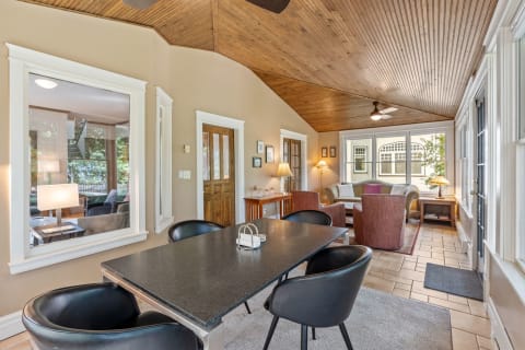 Interior view of a dining area with a black table and stylish chairs leading into a living area adorned with soft seating and large windows.