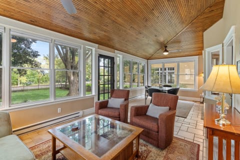 A bright sunroom with wooden ceilings, large windows, and comfortable seating.