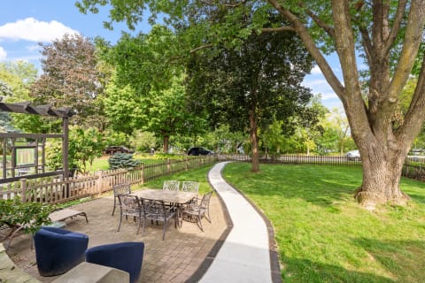 A cozy patio with a stone dining table and chairs surrounded by greenery on a sunny day.