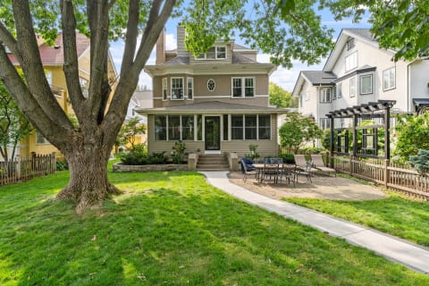 A two-story home with a large front porch, lush lawn, and patio area in a residential setting.