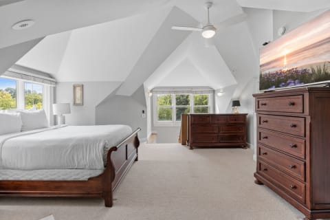 Interior view of a bright attic bedroom with wooden furniture and large windows.