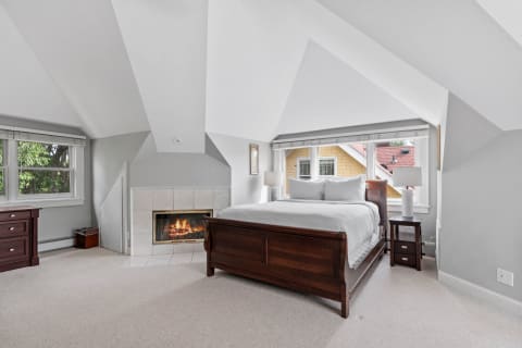 Cozy attic bedroom with vaulted ceilings and a fireplace.