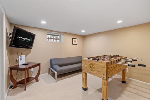A game room featuring a foosball table, a gray sofa, and a TV mounted on the wall.