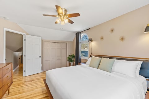 A cozy bedroom featuring a bed with white linens, a decorative window, and wooden accents.