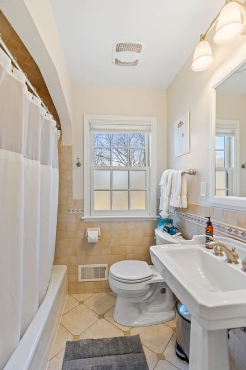 A well-lit bathroom featuring a shower, toilet, and sink, highlighted by a frosted window and beige tiles.