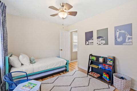 A children's bedroom featuring a turquoise bed, colorful toys, and framed construction vehicle art.