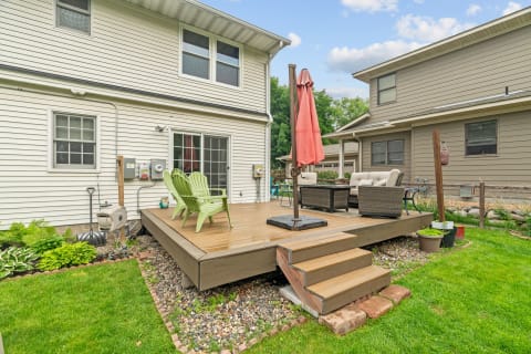 A backyard deck with light green chairs, a coral umbrella, and a cozy seating area.