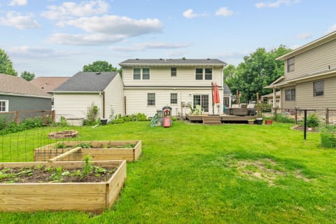 A lush green backyard featuring a wooden deck, raised garden beds, and a two-story house in the background.