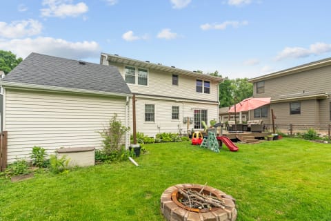 Backyard scene with a fire pit, slide, toy car, and patio seating area under an umbrella.