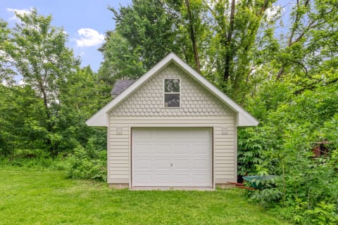 A light-colored garage with a gabled roof, set amidst dense greenery.