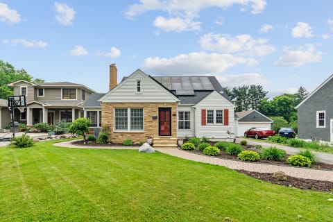 A charming home with a red door, solar panels, and vibrant landscaping in a suburban setting.