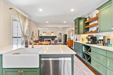 A spacious kitchen featuring green cabinets, a farmhouse sink, and a dining area in the background.