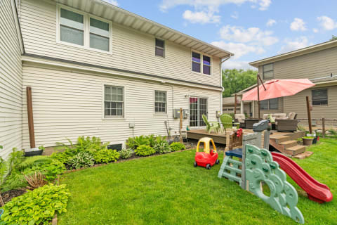 A backyard featuring a playset, a toy car, and a comfortable seating area under an umbrella.