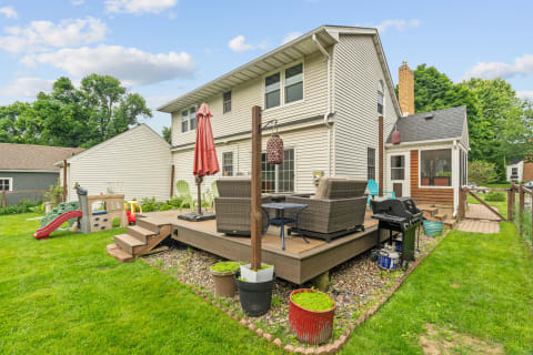 Backyard view featuring a wooden deck with chairs, a play structure, and a grill.