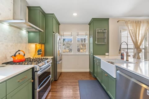 Modern kitchen with green cabinets, stainless steel appliances, and an orange kettle.