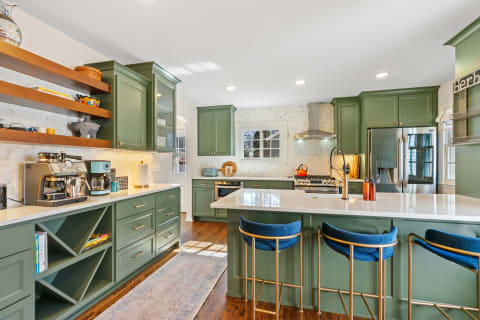 A contemporary kitchen featuring green cabinetry, quartz countertops, a coffee station, and blue stools.