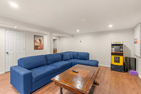 Basement lounge with a blue couch, wooden coffee table, and PAC-MAN arcade game.