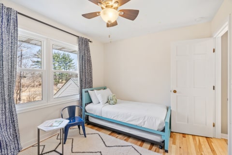 A cozy bedroom with a light blue bed, a blue chair, and large windows.