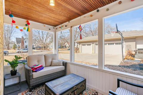 Cozy screened-in porch featuring a beige sofa, colorful decorations, and a view of the outdoors.