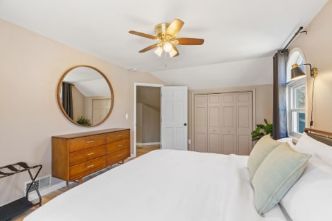 A modern bedroom featuring a bed with white linens, a wooden dresser, and a round mirror.