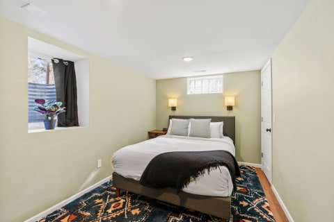 A modern bedroom featuring a neatly made bed and a window nook with a plant.