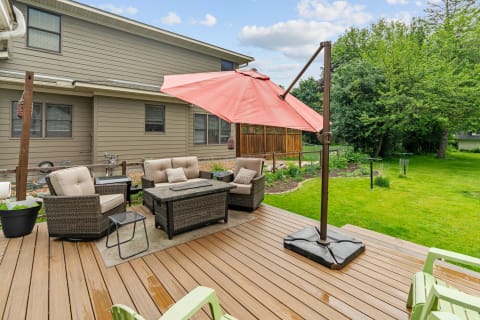 Patio with wicker furniture, pink umbrella, and lush backyard greenery.
