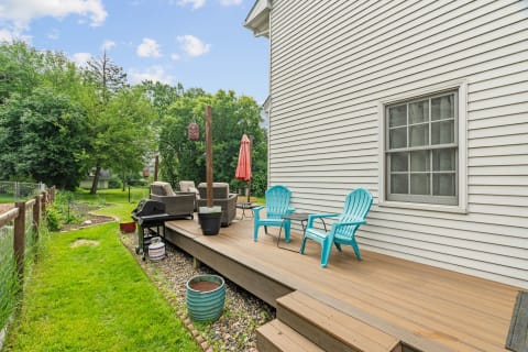 A view of a wooden deck with blue chairs and a grill in a green backyard.