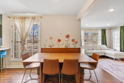 A dining area featuring a wooden table, leather chairs, and a floral wall mural with a view outside.