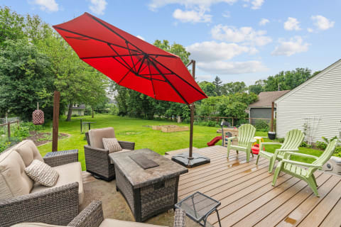 An outdoor patio deck with a red umbrella, wicker chairs, and a view of a green lawn.