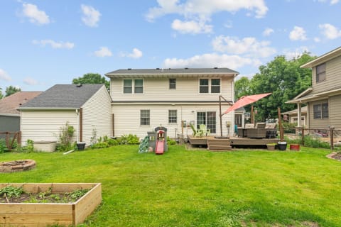 Backyard view of a two-story house with a green lawn, deck, and playground slide.