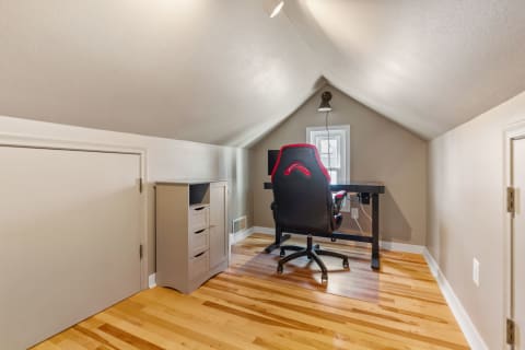 Cozy home office in an attic with a sloped ceiling, featuring a desk and ergonomic chair.