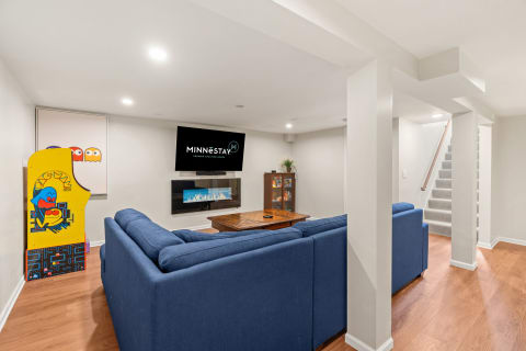 Basement living room with blue couch, electric fireplace, and arcade game.