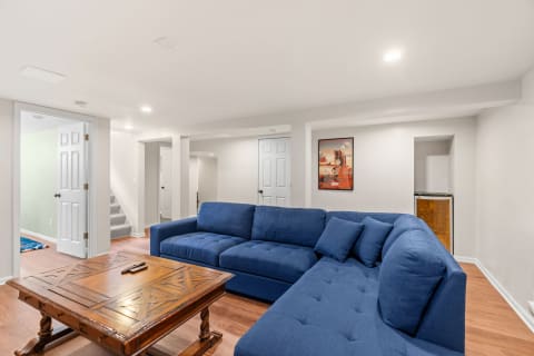 Spacious basement with a blue sectional couch, wooden coffee table, and decorative poster.