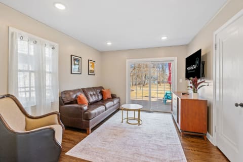 A warm and inviting living room featuring a leather sofa, accent chair, and glass door leading to a deck.