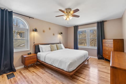 Spacious bedroom with a bed, nightstand, dresser, and large windows.