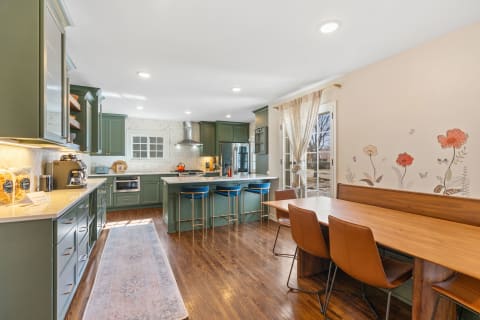 A contemporary kitchen with green cabinetry, wooden flooring, and a floral wall mural.