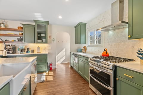 A bright kitchen with green cabinets and modern appliances, featuring wood floors and natural light.
